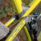 Close-up of a yellow mountain bike frame with the model name 'Truffle-120' printed on the down tube, set against a blurred outdoor forest background.