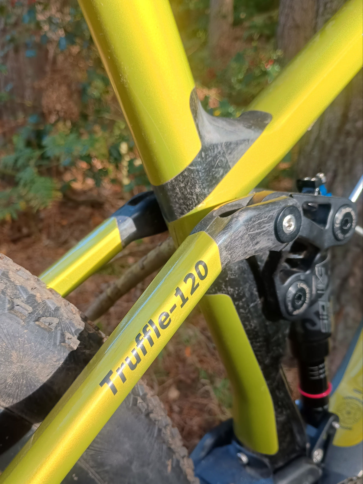 Close-up of a yellow mountain bike frame with the model name 'Truffle-120' printed on the down tube, set against a blurred outdoor forest background.