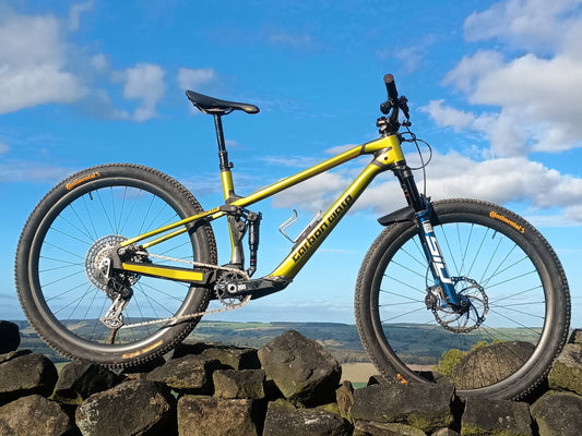 A yellow and black full-suspension mountain bike is photographed outdoors on a stone wall under a bright blue sky with white clouds.